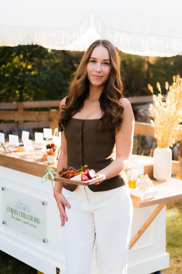 Sarah Jean, founder of Cured Creations by Sarah, styling her luxury bespoke charcuterie cart at an outdoor Edmonton event